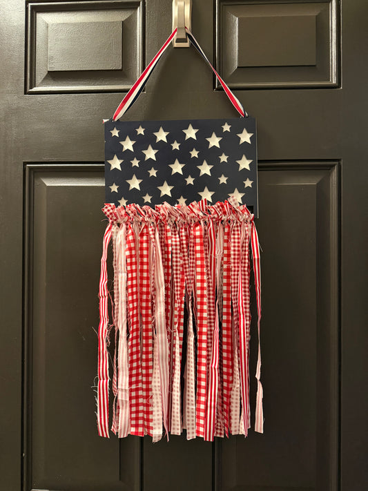 Decorative American flag wall hanging with red and white checkered fabric on a dark door.