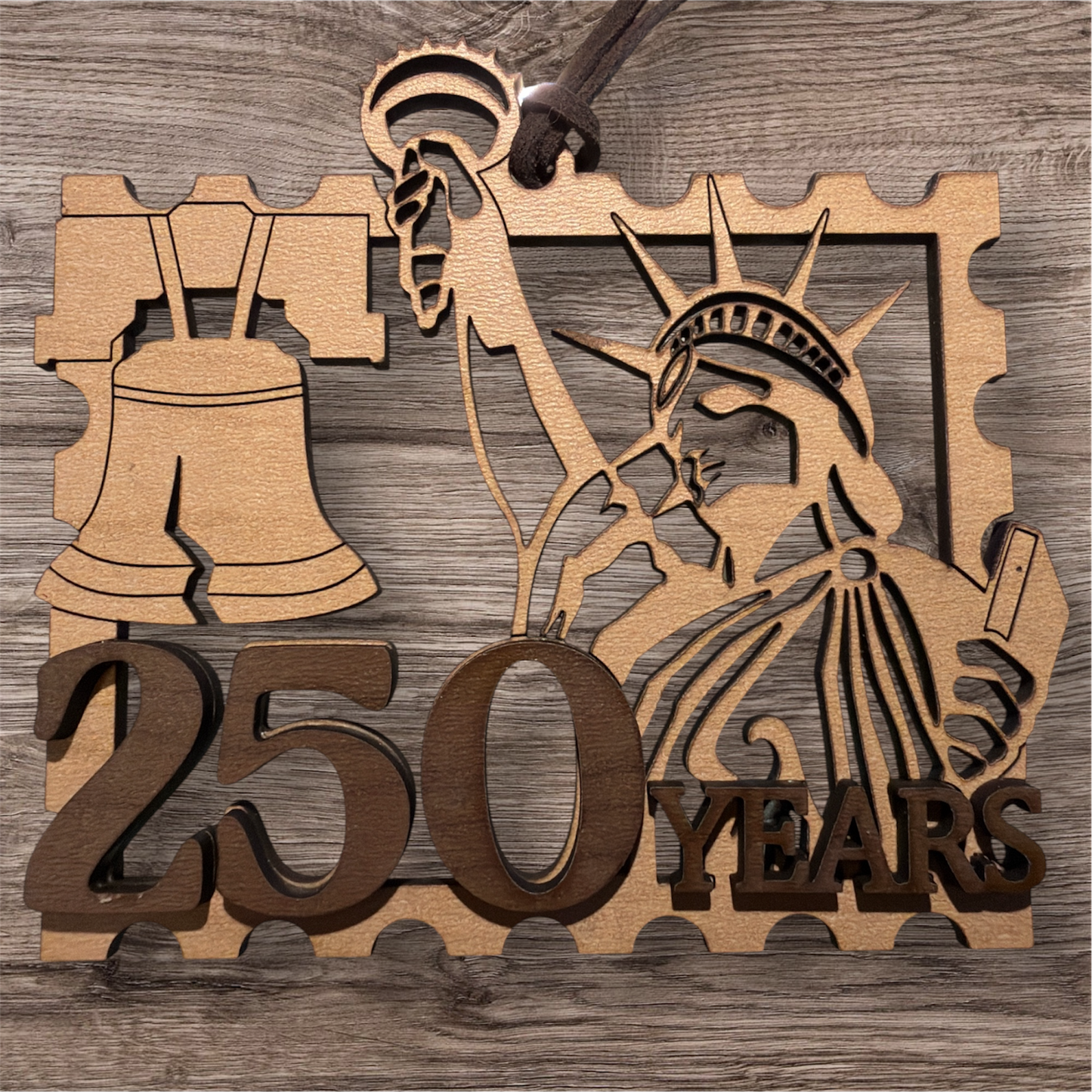 Wooden plaque with Liberty Bell and Statue of Liberty design celebrating 250 years on a wooden background.