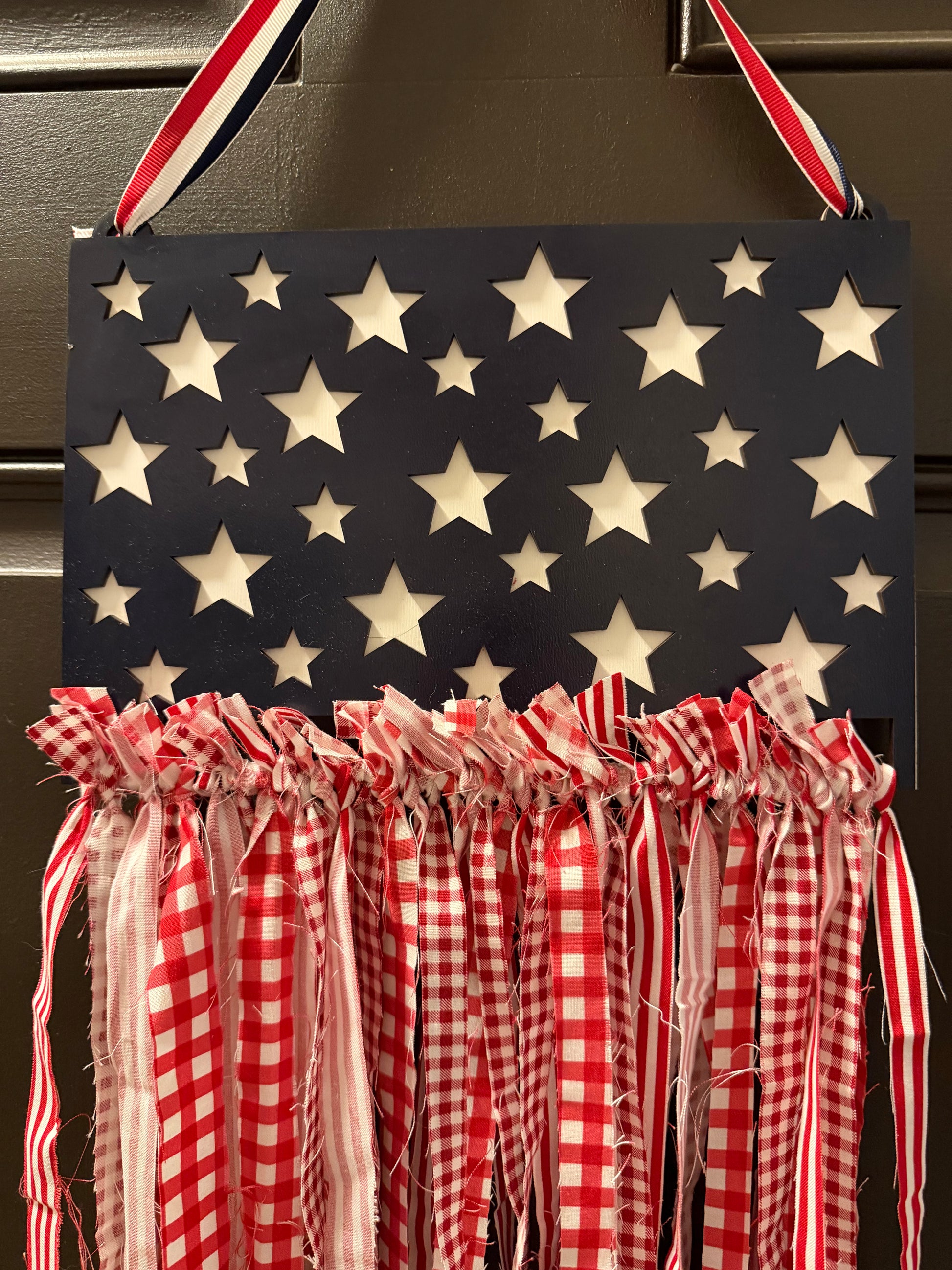Decorative sign with American flag pattern and red checkered ribbons hanging on a door.