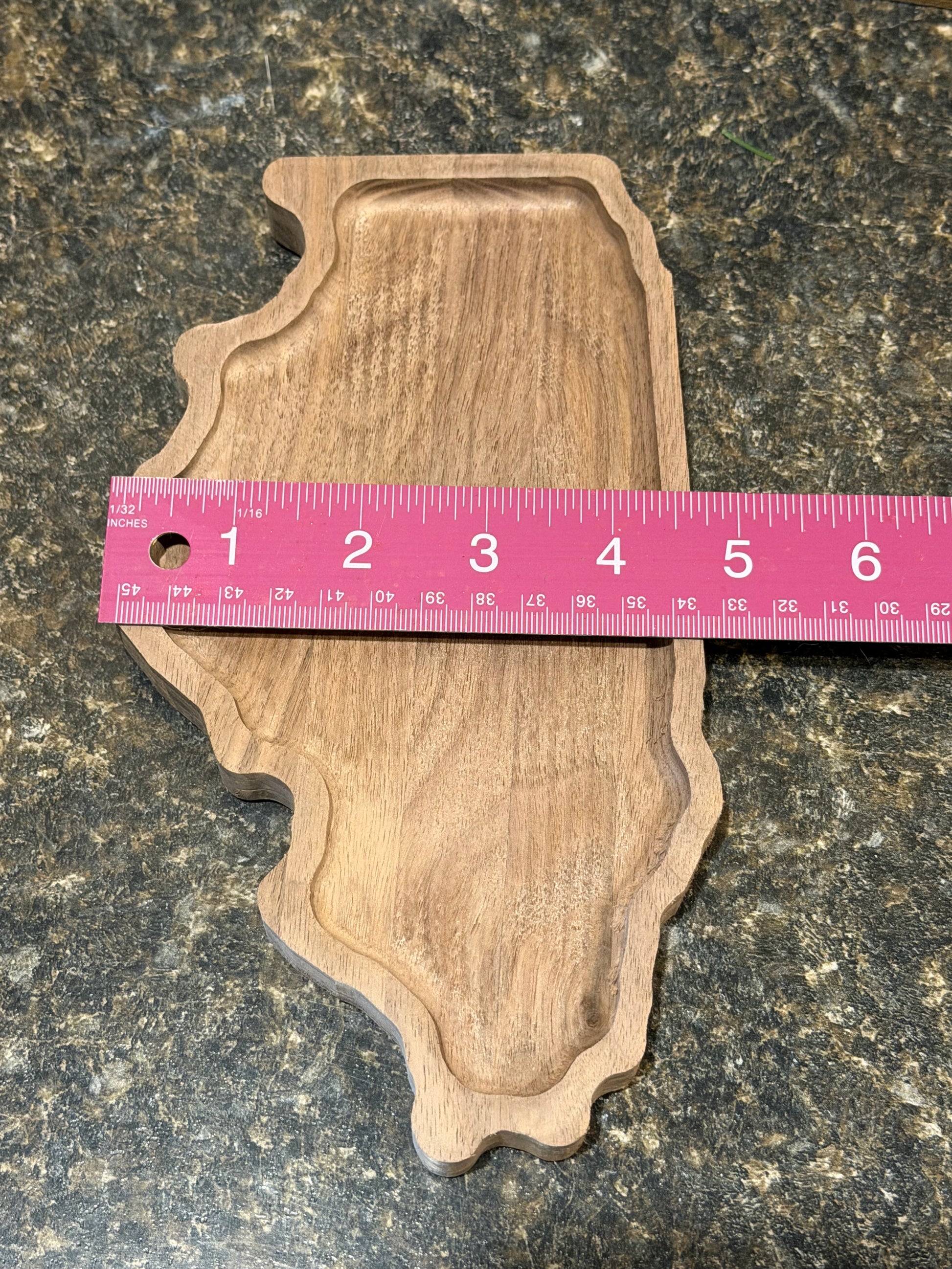 Wooden tray shaped like the state of Illinois with a pink ruler for scale on a dark surface- measuring 4.5" across.