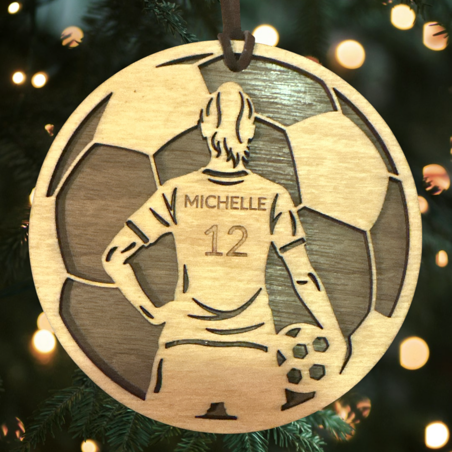 Wooden ornament with a silhouette of a person wearing a jersey labeled 'Michelle' and the number '12', hanging on a Christmas tree.
