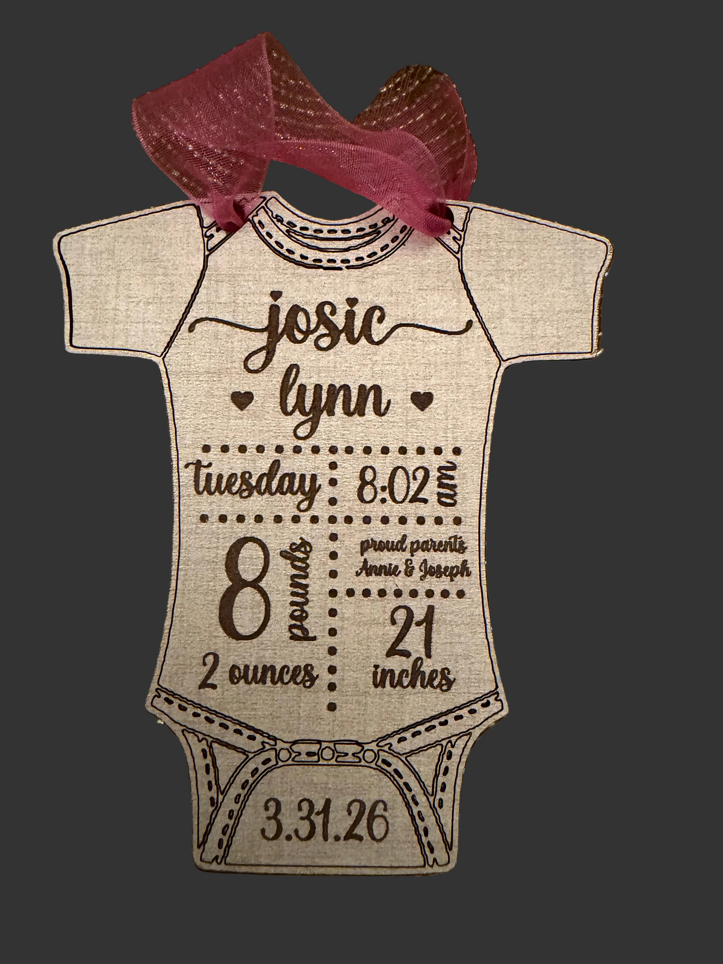 Wooden baby onesie-shaped ornament with engraved text on a textured surface